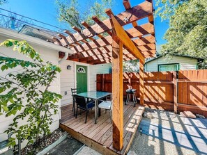 Une terrasse en bois avec une pergola, une table et des chaises, et une porte verte.