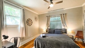 Una camera da letto con un letto, una scrivania, una sedia, una ventola a soffitto e una finestra con tende.