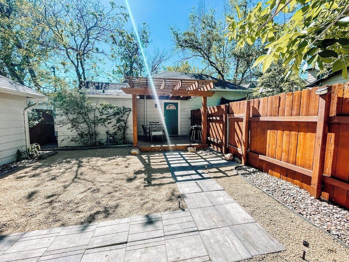 Un patio trasero con un pérgola de madera, una zona de patio y una valla de madera.
