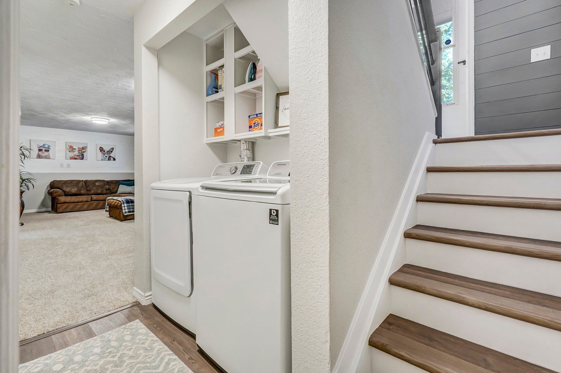 Un lavadero con lavadora y secadora, un estante con productos de limpieza y una escalera con escalones de madera.