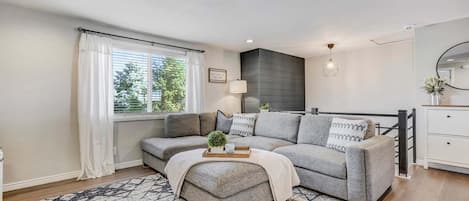 A modern living room with a grey sofa, ottoman, and patterned rug.