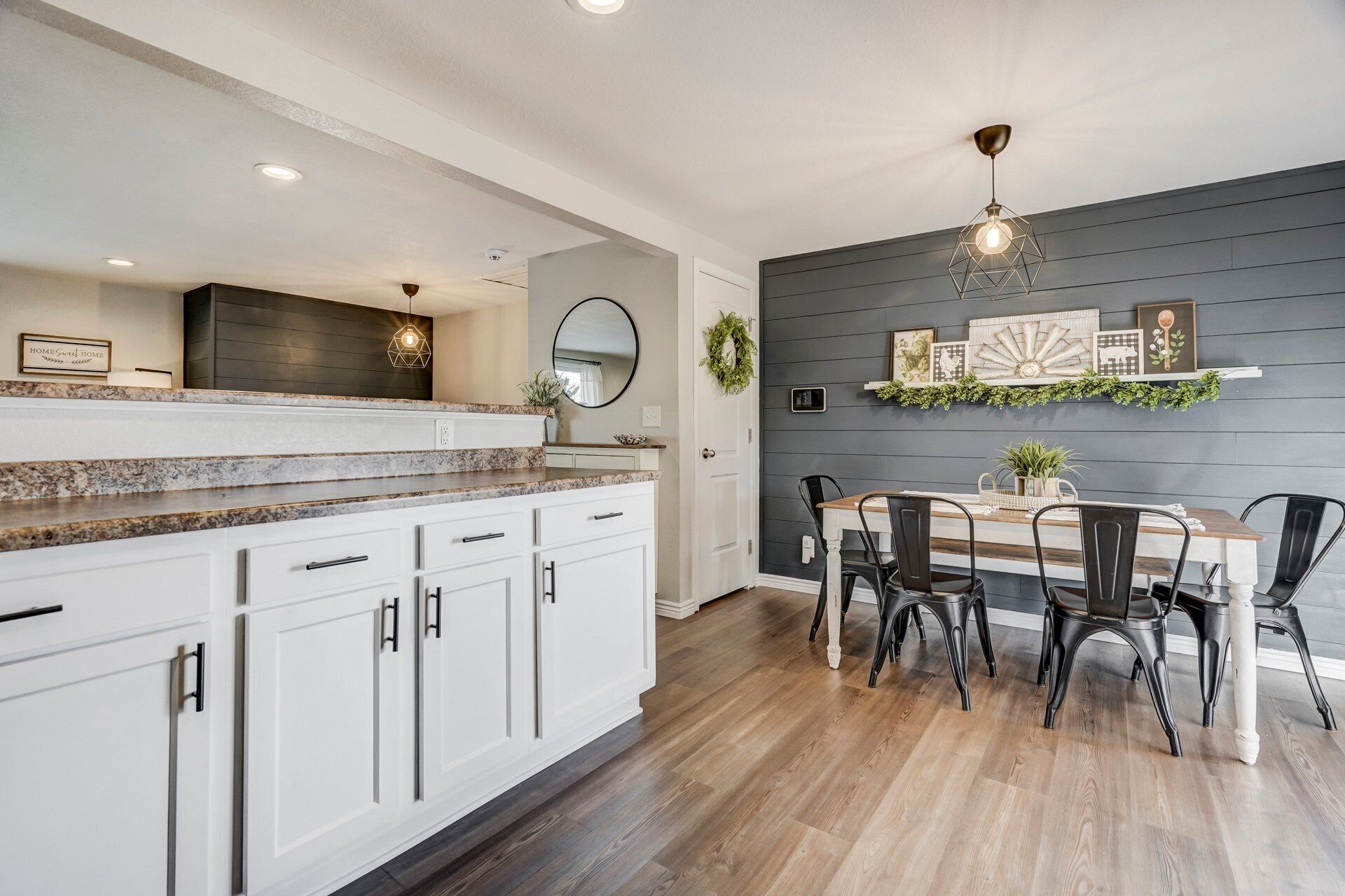 Una cocina con armarios blancos, encimera de granito y comedor con mesa de madera y sillas negras.