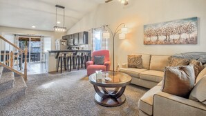A spacious living room with a sofa, a coffee table, and a red armchair. There is a kitchen area in the background with a dining table and chairs. - Hot Tub Retreat Near Fort Carson (Colorado Springs)