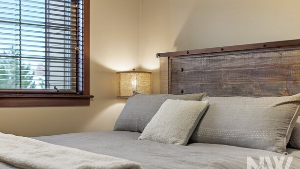 A neatly made bed with a wooden headboard, a bedside lamp, and a window with blinds.