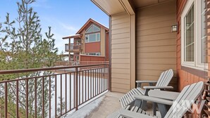 A balcony with a metal railing, two Adirondack chairs, and a view of a two-story building with a balcony.