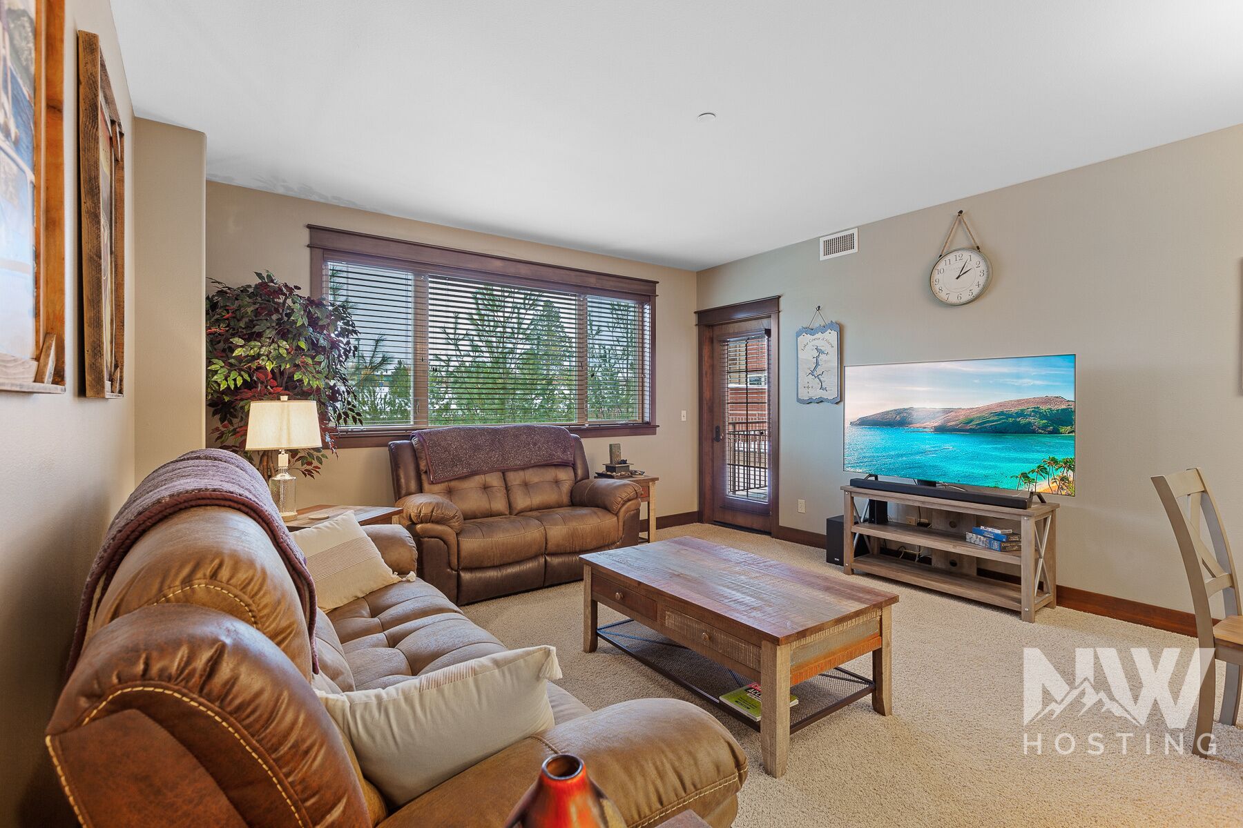 A living room with a leather sofa, a wooden coffee table, a TV on a stand, and a large window with blinds.