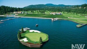 A golf course island with a clubhouse, surrounded by water and forested hills.