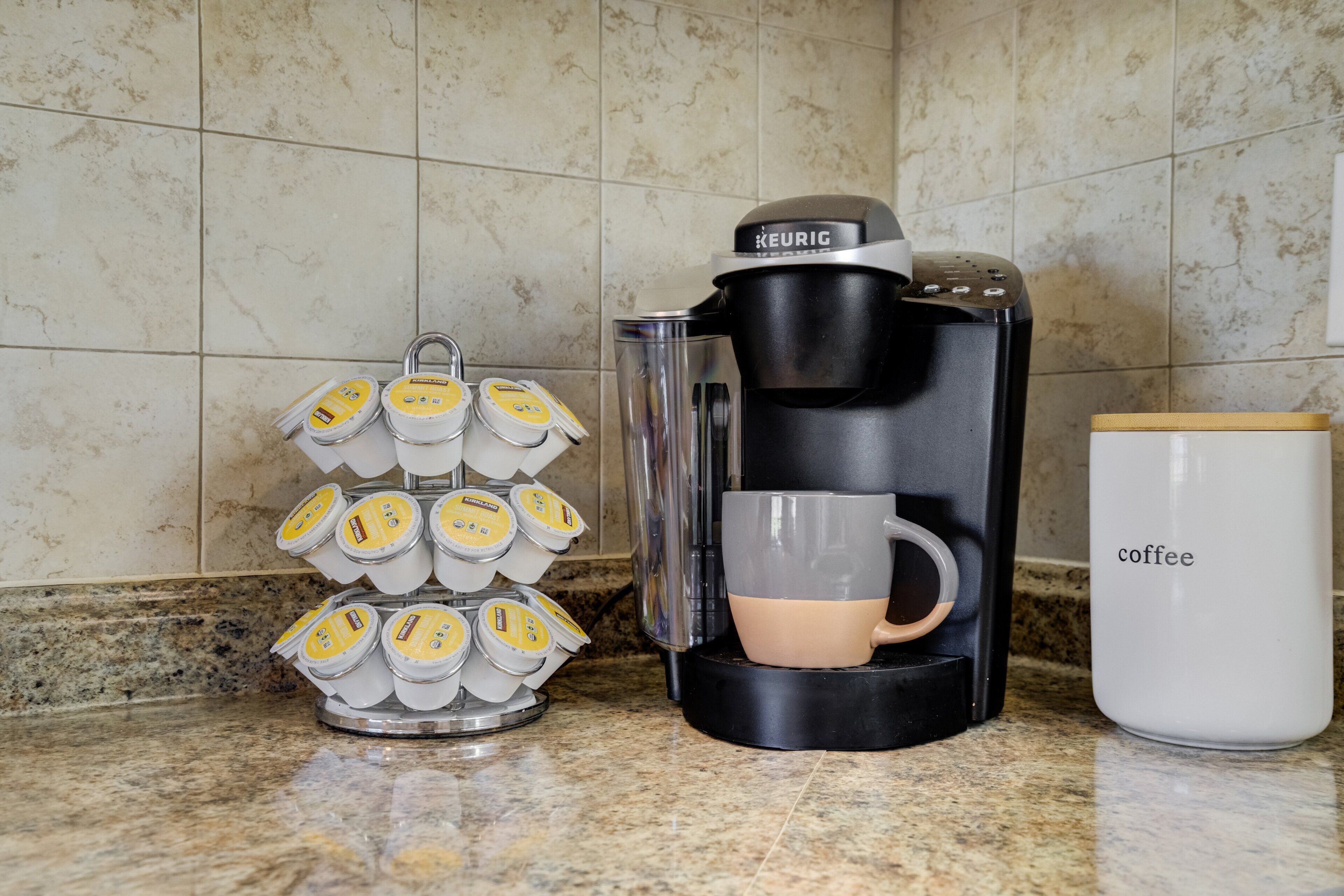 Una cafetera, una taza y un dispensador de cápsulas de café sobre una encimera de cocina.