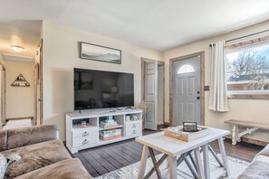 A living room with a flat-screen TV, white furniture, a wooden coffee table, and a view through a door. - One Level Home Near Downtown Hot Tub (Colorado Springs)