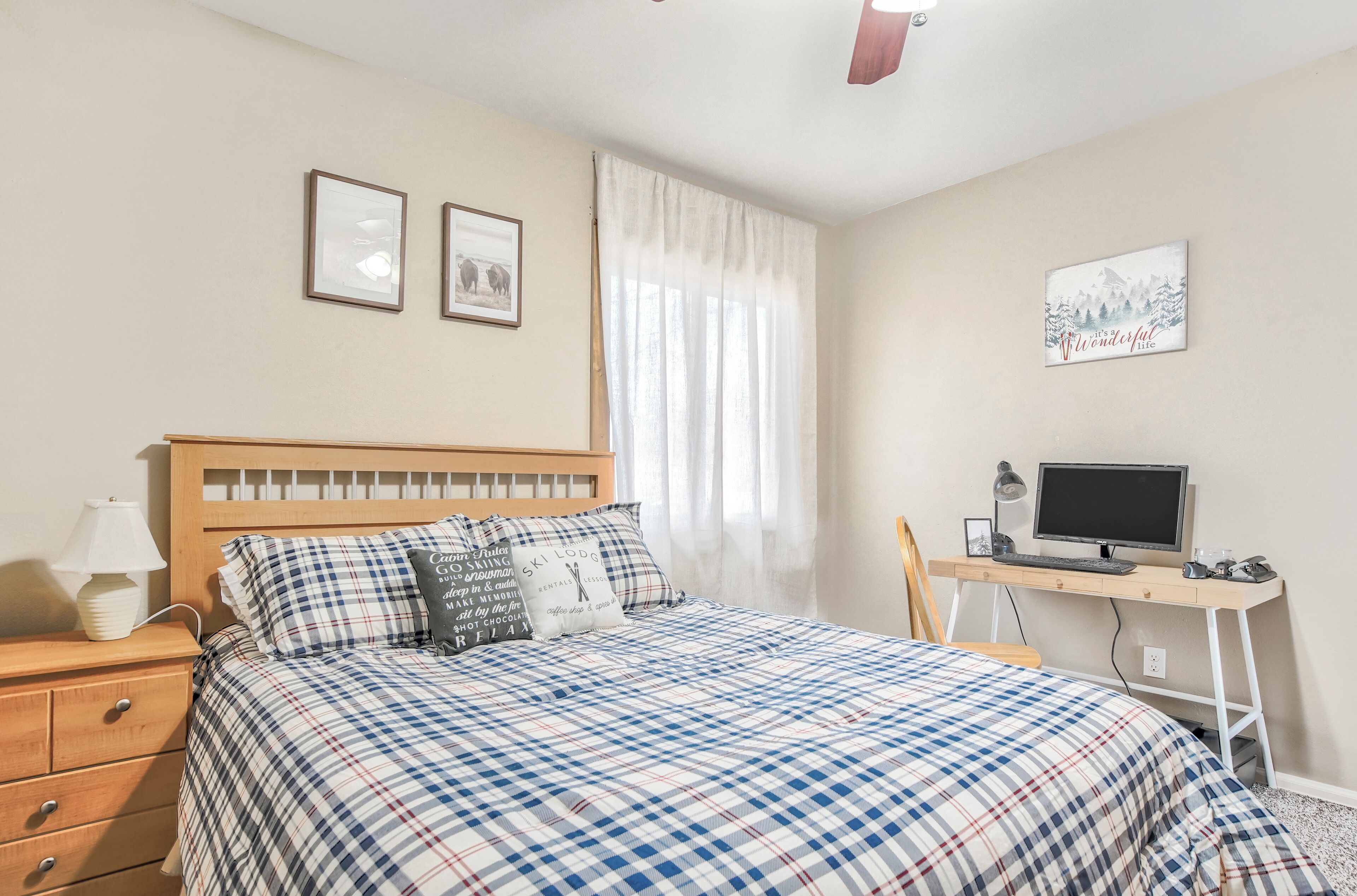 A bedroom with a bed, a desk with a computer, and a window with curtains.