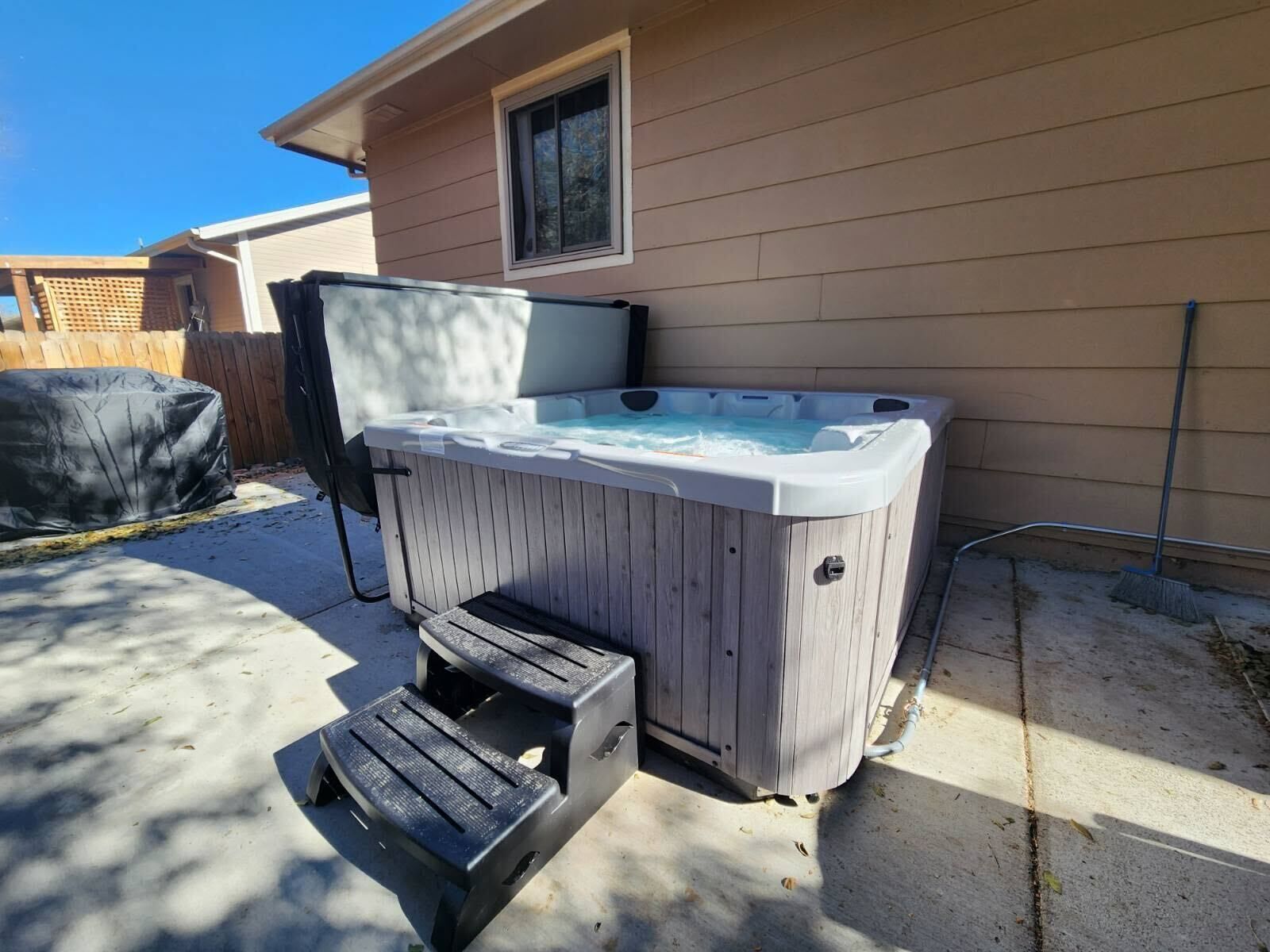 A hot tub in a backyard with a wooden deck and a window.