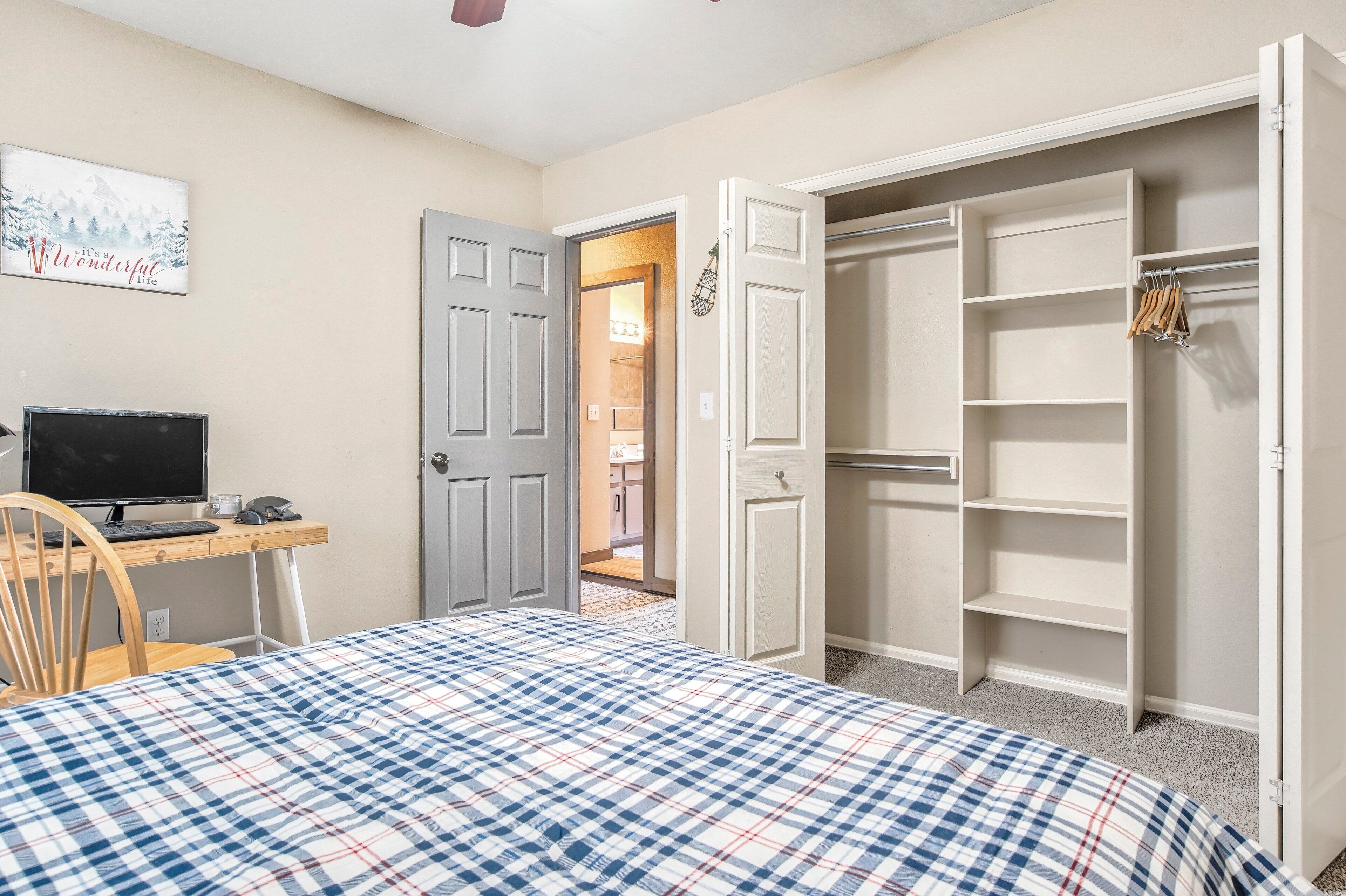 Un dormitorio con colcha a cuadros, un escritorio con computadora, una silla y un vestidor.