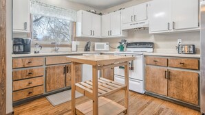 A kitchen with white cabinets, a wooden table, and a ceiling fan. - One Level Home Near Downtown Hot Tub (Colorado Springs)