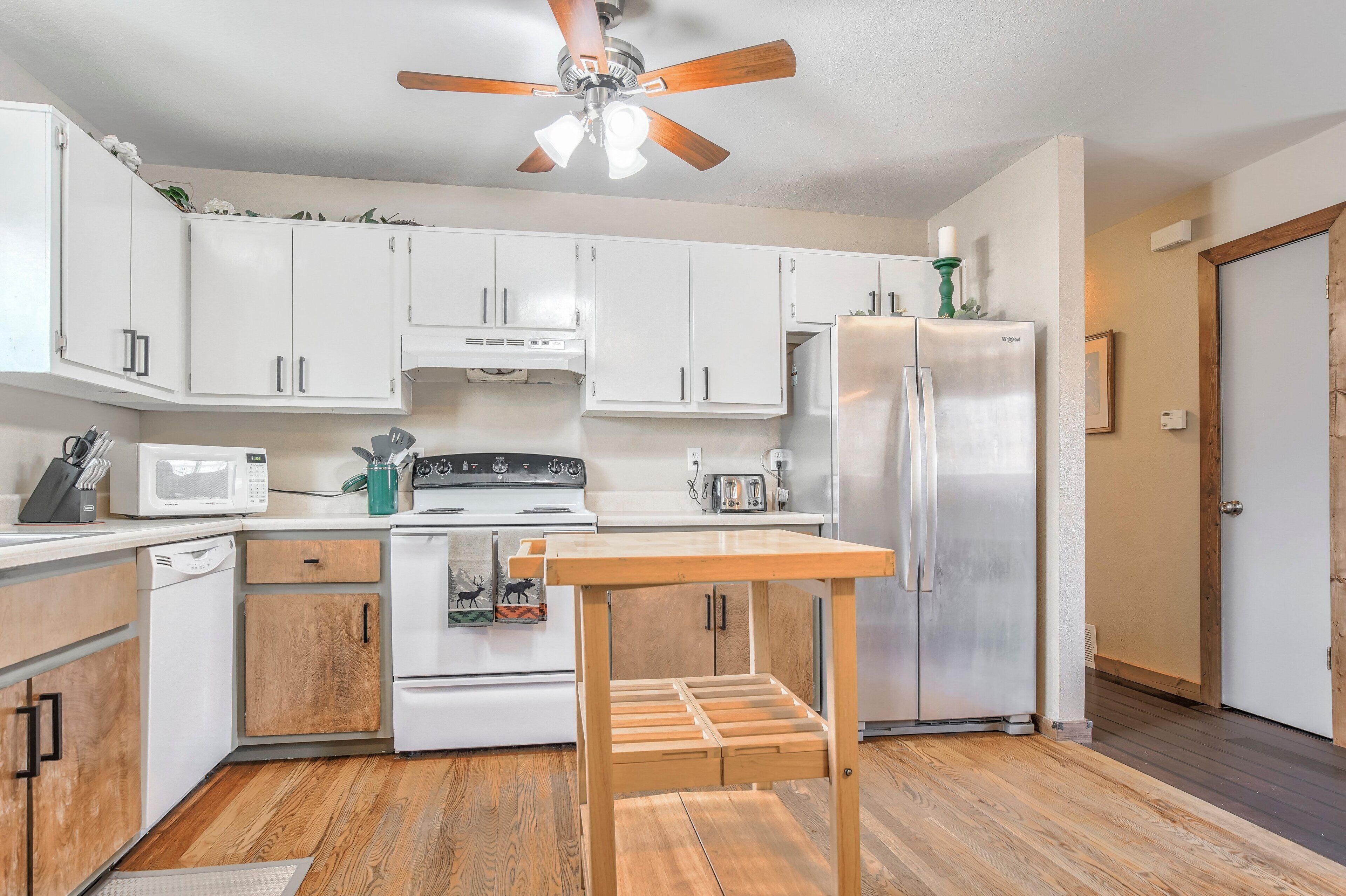 A modern kitchen with white cabinets, stainless steel appliances, and a wooden table.