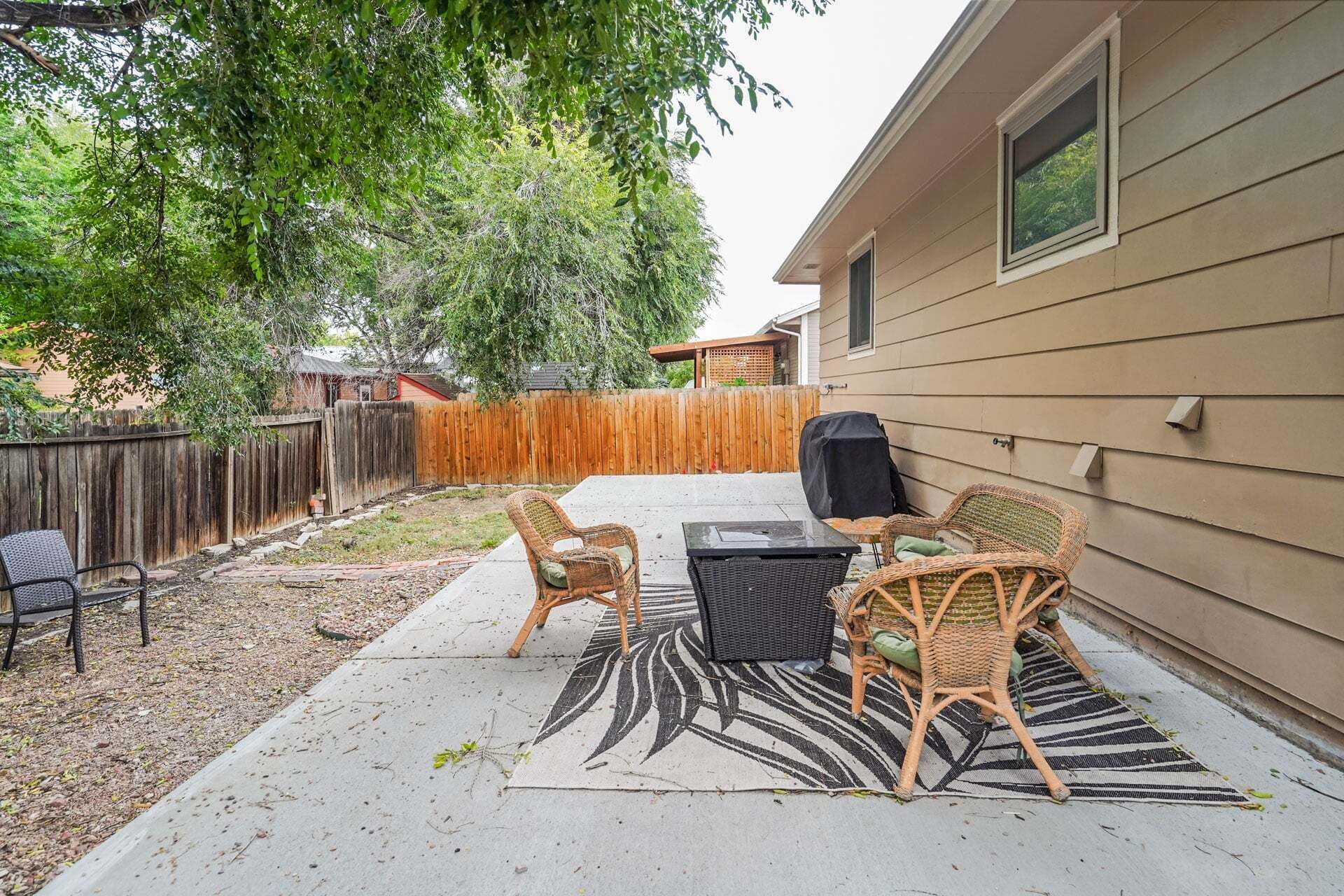 A backyard with a patio, outdoor furniture, a grill, and a wooden fence.