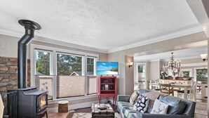 A spacious living room with a fireplace, a television, and a dining area visible through large windows. - Mt 00507 (Coeur d'Alene)