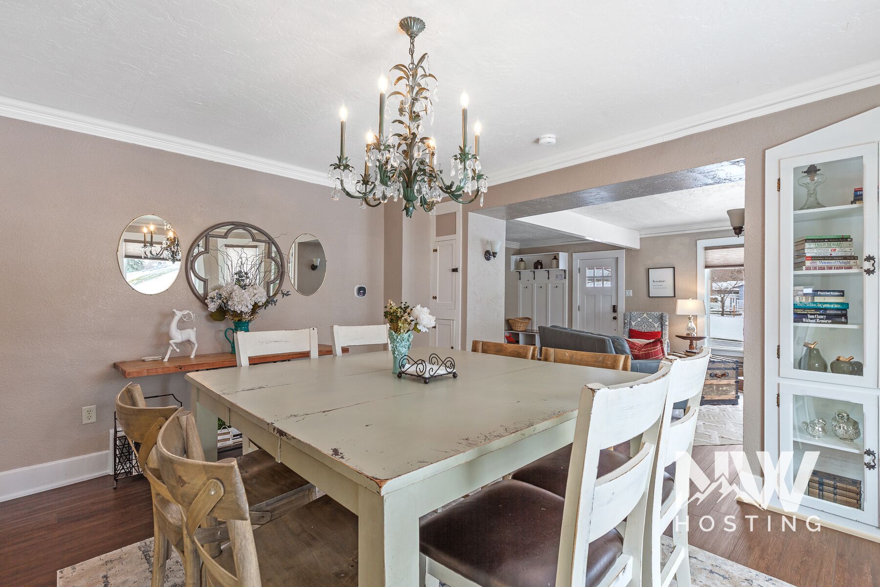 A dining room with a large table, chairs, a chandelier, and a kitchen visible through an open door.