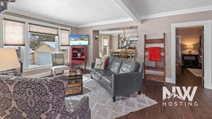 A spacious living room with a grey leather sofa, patterned armchair, and a wooden chest of drawers. A television is mounted on the wall, and a red ladder leans against the wall. - Mt 00507 (Coeur d'Alene)
