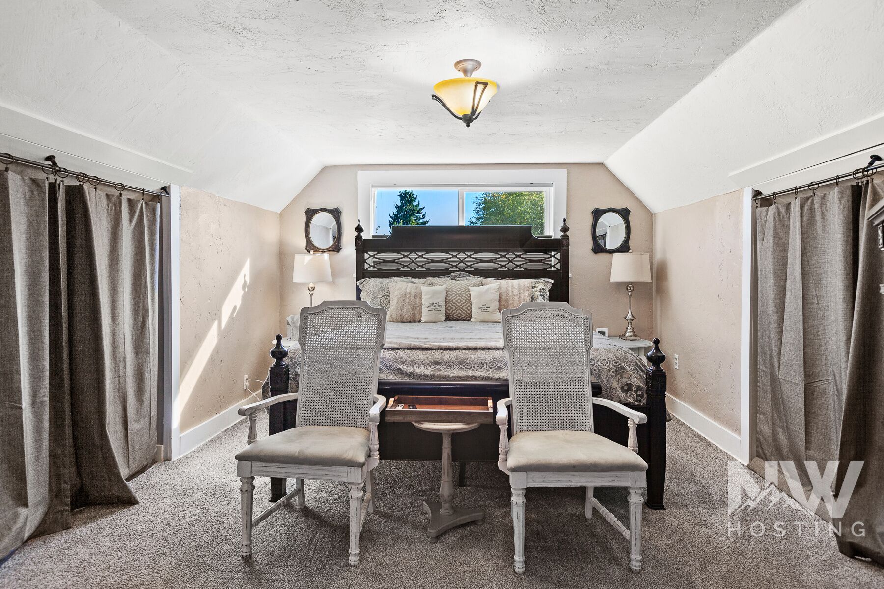 A bedroom with a bed, two chairs, a window, and a ceiling light.