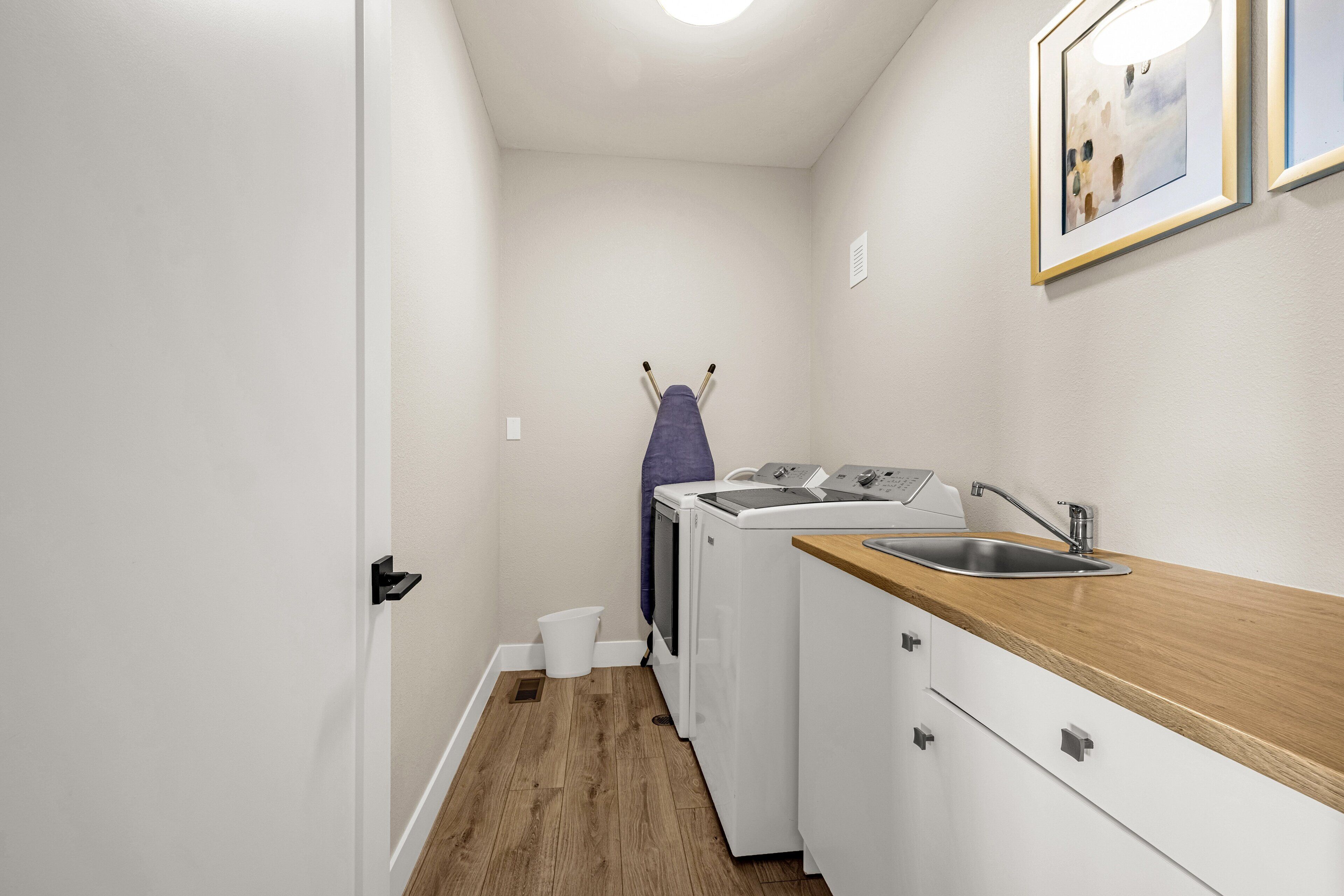 A compact laundry room with a washing machine, dryer, sink, and wooden countertop.