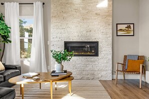 A living room with a brick wall, a fireplace, a sofa, a coffee table, and a chair. - Mountain Retreat With Hot Tub & Views (Colorado Springs)