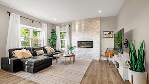A modern living room with a black leather sofa, a wooden coffee table, and a stone fireplace wall. - Mountain Retreat With Hot Tub & Views (Colorado Springs)