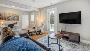 A living room with a sofa, a coffee table, a TV mounted on the wall, and a door leading to another room. - Downtown Getaway With Balcony King Beds (Colorado Springs)