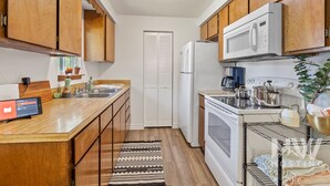 A compact kitchen with wooden cabinets, a white refrigerator, a microwave, a stove, and a sink. - Dt 01906 (Coeur d'Alene)