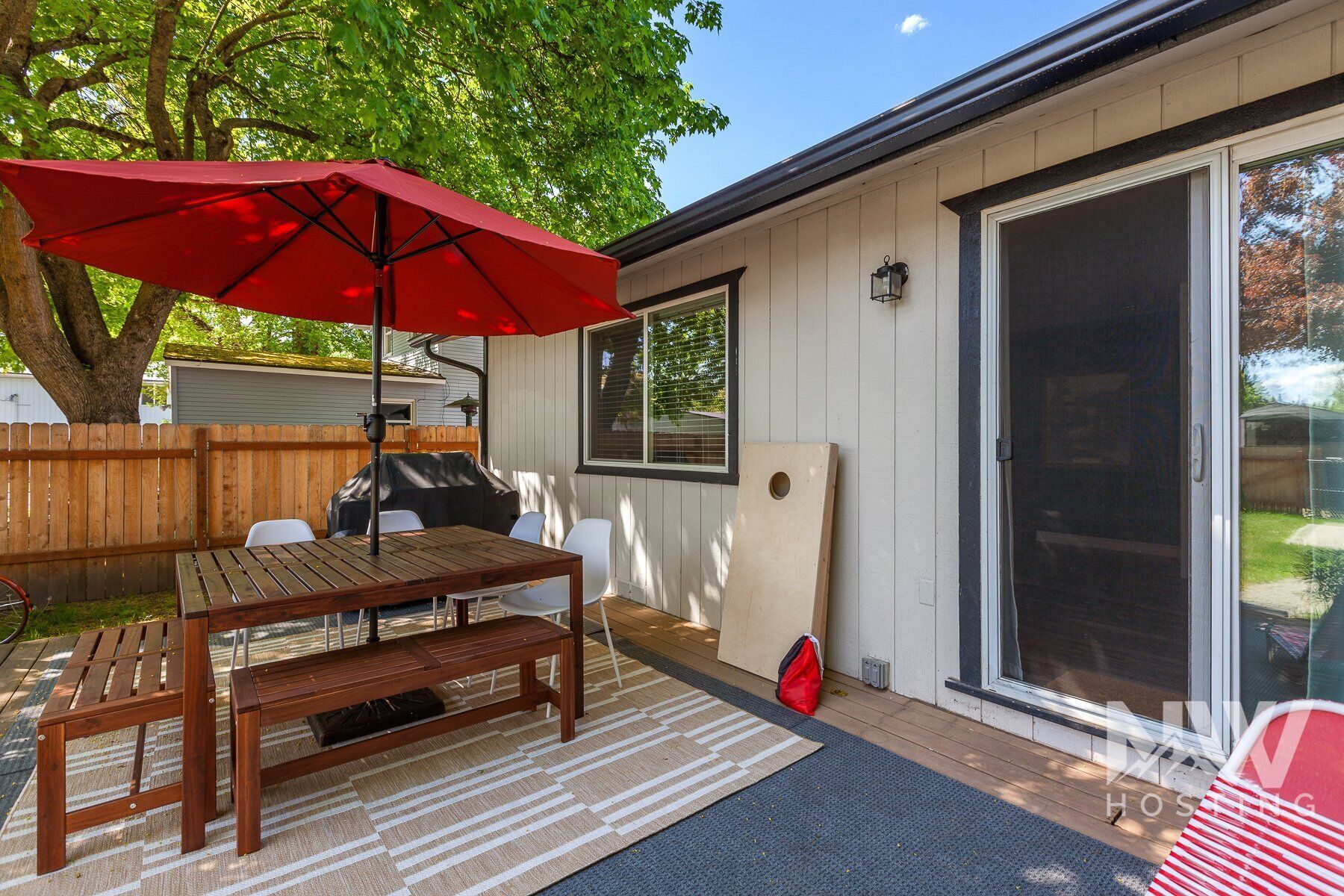 A patio with a wooden table and chairs, a red umbrella, and a sliding glass door.