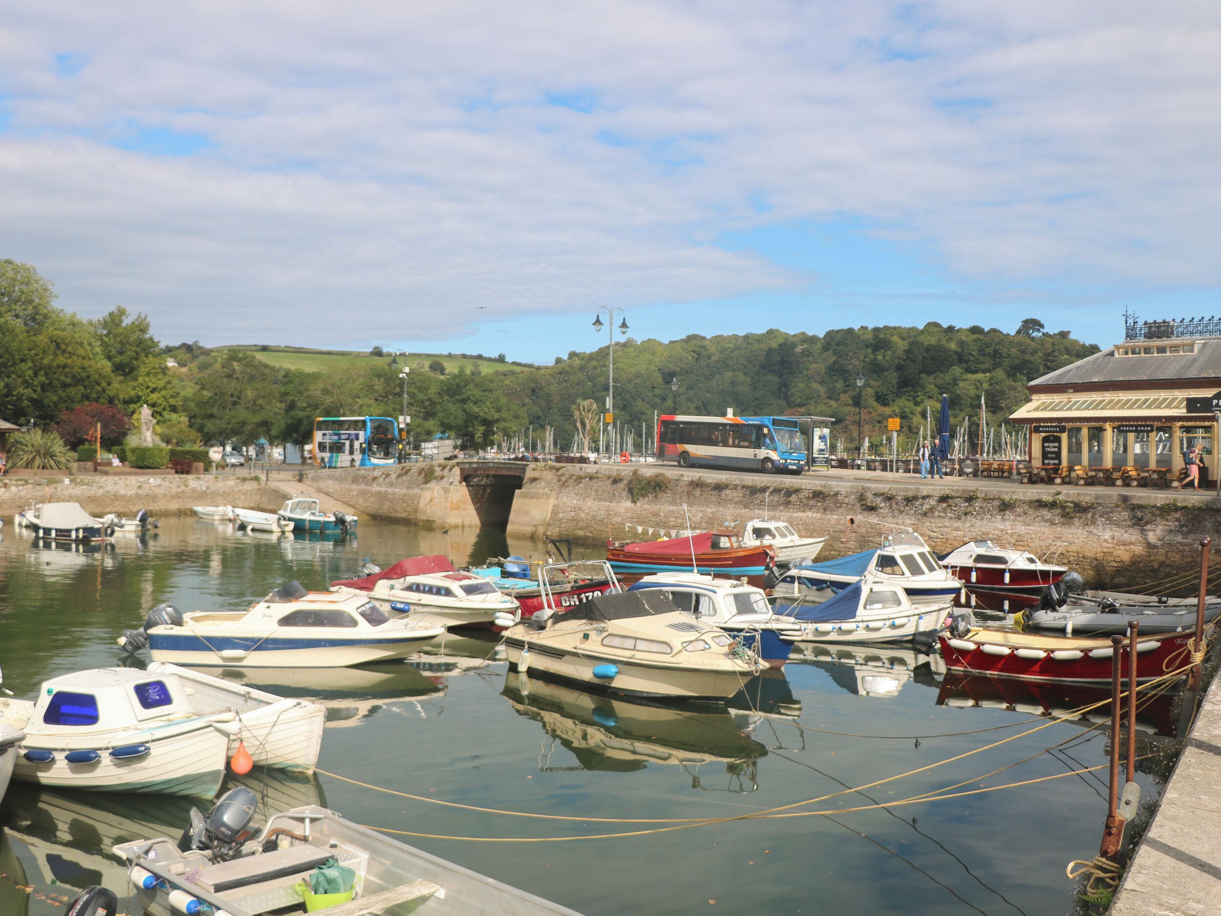 A marina with various boats docked, a bus, and a building with a sign.