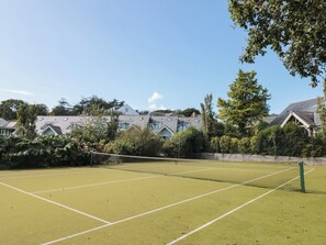 Tenniskenttä, jossa on verkko, ja jonka ympärillä on puita ja taloja.