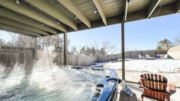 A hot tub under a covered area with a wooden deck, a wooden chair, and a wooden fence in the background. - Sunset Mesa Hideaway With Hot Tub (Colorado Springs)