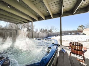Ein Whirlpool unter einem Vordach mit Holzterrasse, einem Holzstuhl und einem Holzzaun im Hintergrund.