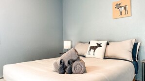 A neatly made bed with a white comforter, a pair of folded slippers, and two pillows with a moose design. - Sunset Mesa Hideaway With Hot Tub (Colorado Springs)