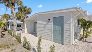 A single-story building with a green door, a small porch, and a gravel driveway. - Welcome to The Drift Your Laid-back Beach Escape in Cocoa Beach! (Cocoa Beach)