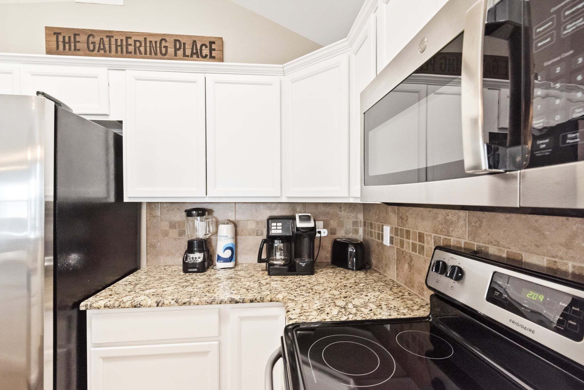 A kitchen with white cabinets, a black refrigerator, a coffee maker, a toaster, and a stove.