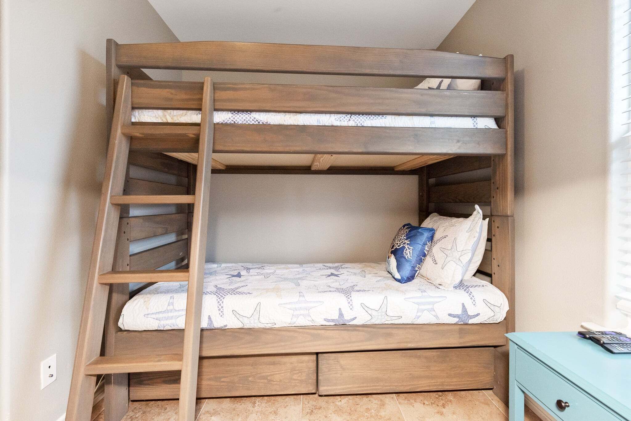 Una cama litera con escalera de madera, un colchón con motivos de estrellas y una almohada azul.