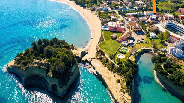 Vista aérea de un pueblo costero con playa, edificios residenciales y un promontorio rocoso.