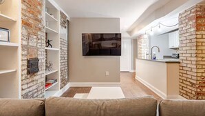 Ein modernes Wohnzimmer mit einer Ziegelfassade, einem flachbildfernseher über einem Kamin und einer Küchenzeile mit Ziegelrückwand.