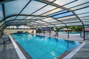 Una piscina interna con tetto in vetro, circondata da sedie a sdraio e un patio coperto.