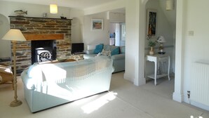 A living room with a stone fireplace, a sofa, a television, and a dining area with a table and chairs. - Mount Pleasant (Padstow)