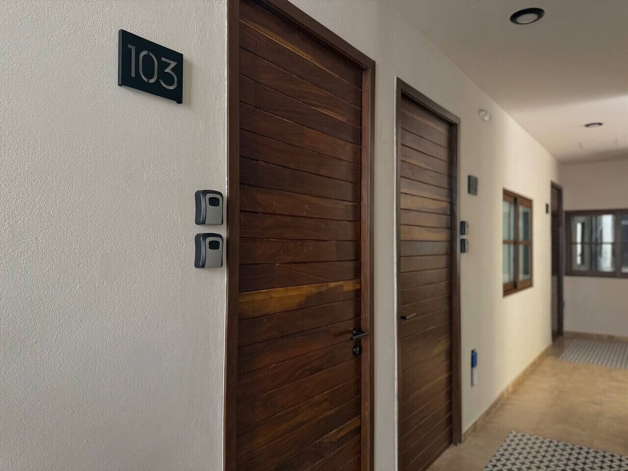 A hallway with two wooden doors, a number sign '103', and a small window.