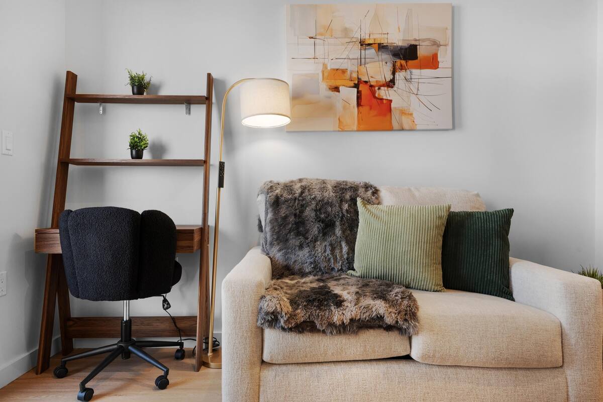 A modern living room with a sofa, a black office chair, a wooden ladder, and a floor lamp.