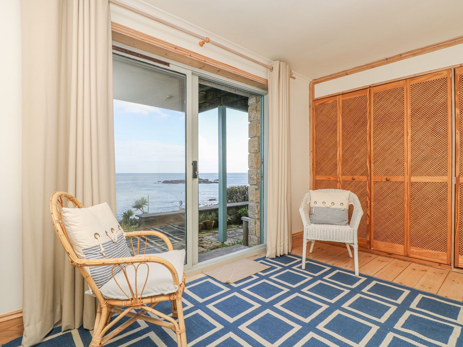 A balcony with wicker chairs, a view of the sea, and a wooden wardrobe.
