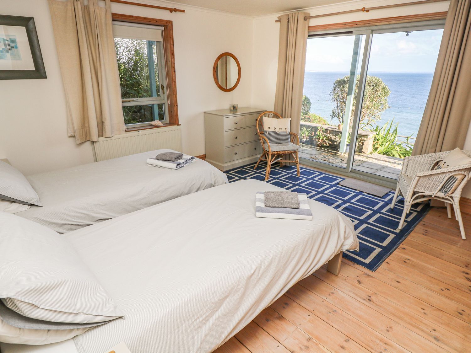 Une chambre avec deux lits, une commode, une chaise et une vue sur la mer.