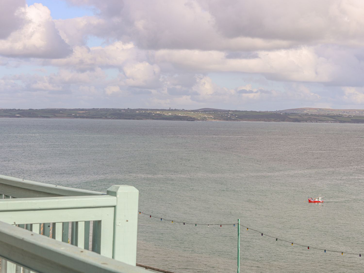 A coastal view with a calm sea, a distant shoreline with buildings, and a red boat in the water.