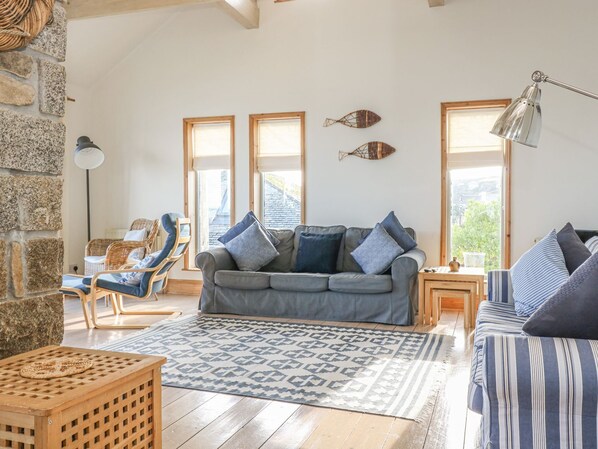 Un salon chaleureux avec un canapé gris, des coussins bleus, un tapis à motifs et un mur en pierre.