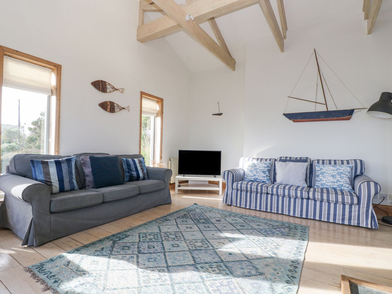 A spacious living room with a grey sofa, a striped sofa, a TV stand, and a patterned rug.