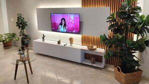A modern living room with a flat-screen TV mounted on a white wall, a wooden accent wall, and a variety of potted plants. - Your comfortable, elegant, and centrally located space with balcony 401 (Medellín)