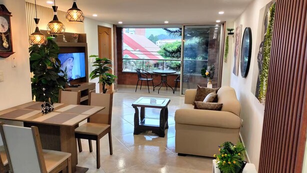 A modern living room with a sofa, dining table, and chairs. There is a television on the left, and a balcony with a view of the outside. - Exclusive, luxurious, centrally located apartment — serene and comfortable 302 (Medellín)